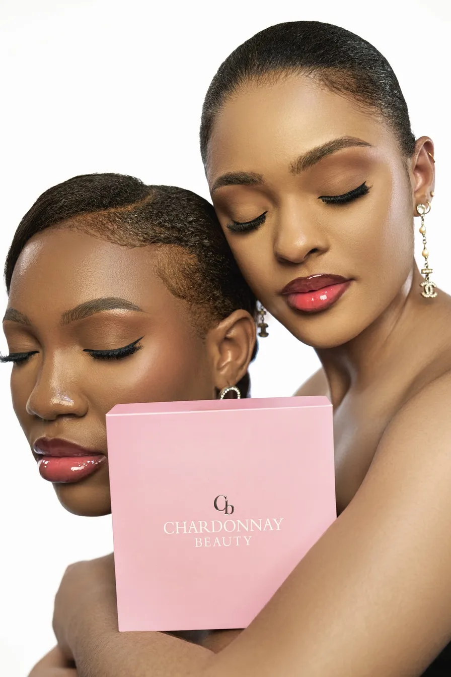 Two models resting together, one holding the pink Chardonnay Beauty box