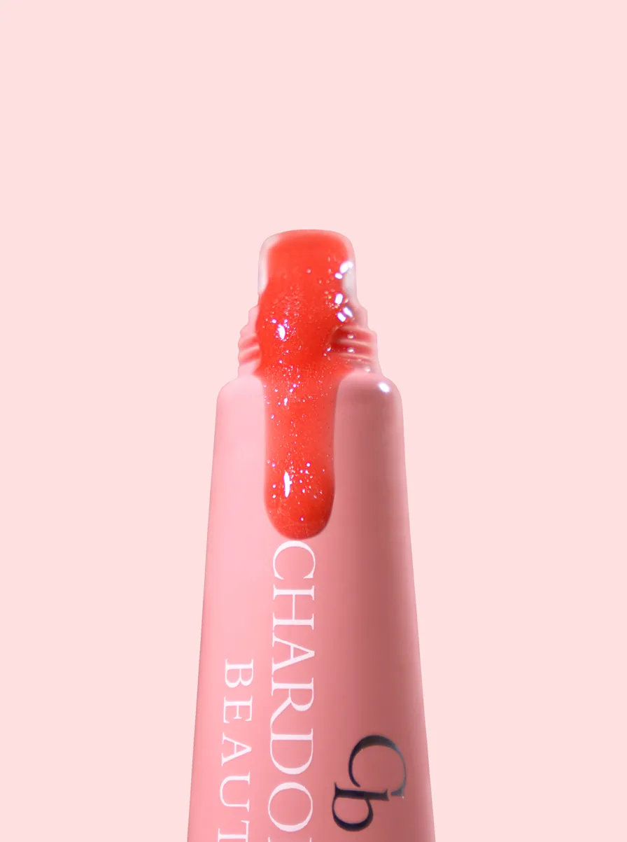 A pink Chardonnay Beauty tube with a shimmering coral-pink gloss catching the light on its applicator
